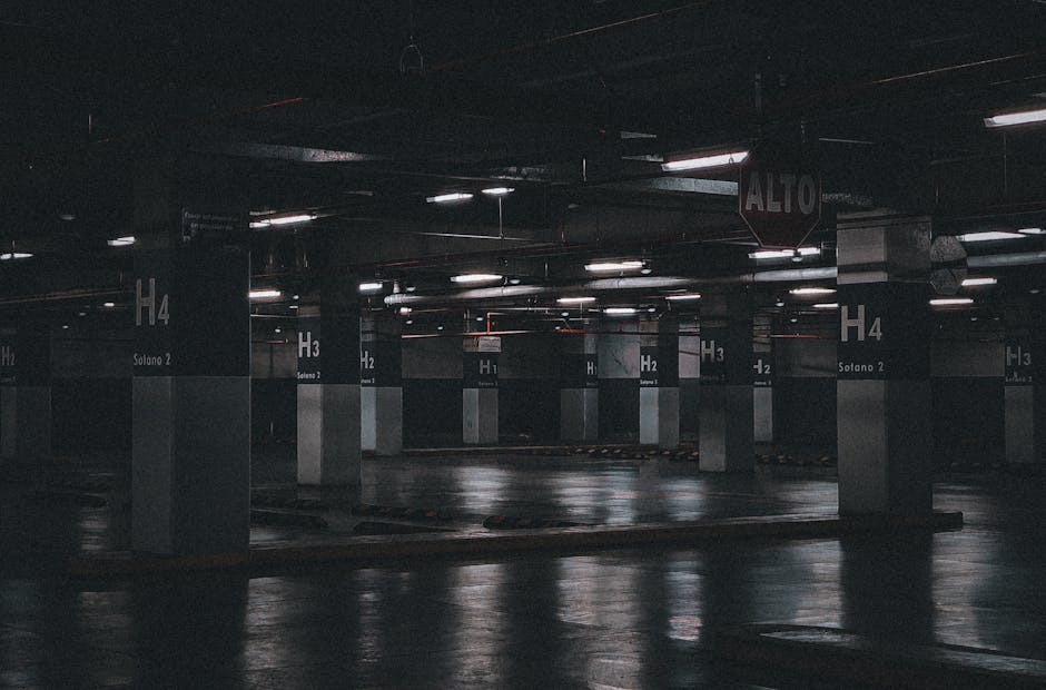 An underground parking garage illuminated by overhead fluorescent lights, showing multiple concrete columns labeled with large white characters such as 'H 4', 'H 3', and 'H 2', each column also marked