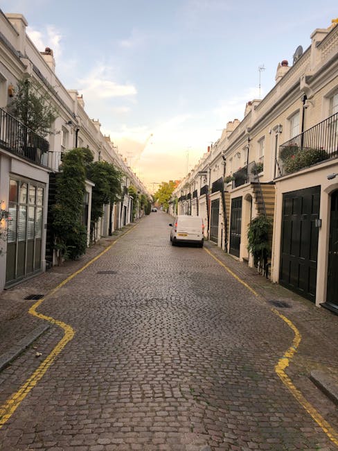 A narrow cobbled courtyard lined with white Victorian-style terraced houses, featuring small front gardens and potted plants arranged along the edges. The buildings have large sash windows, some with 